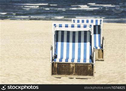 Wicker beach chairs on white sand at North Sea, on Sylt island, in Germany. Summer vacation with blue water, waves and beach chairs. Sunny beach day