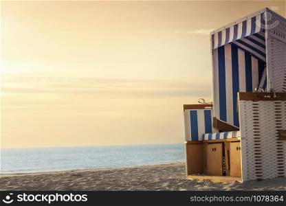 Wicker chair on a beach, at sunset, at the North Sea, on Sylt island, Germany. Summer vacation background. Golden hour beach scenery. Frisian beach.