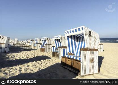 Wicker chairs on beach, aligned, on Sylt island, at North Sea, Germany. Beach scenery on a hot day of summer.