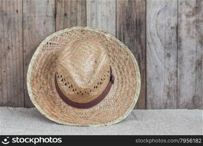 Wicker hat on brown fabric lean against wooden background,