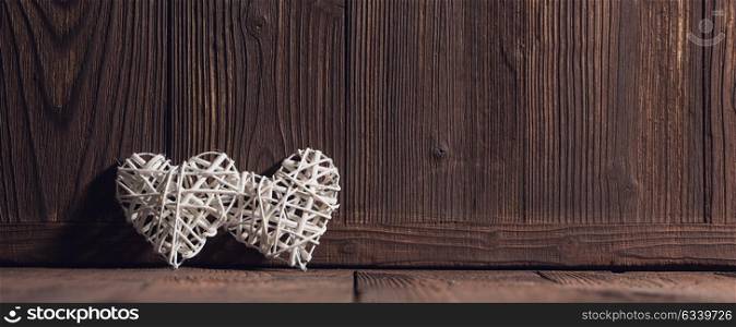 Wicker hearts on wood. Two wicker hearts on brown wooden background