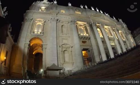 Wide and low angle shot of a girl coming to St. Peters Basilica at night and taking photos with tablet computer. World famous Catholic church