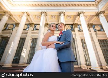 Wide angle portrait of happy bride and groom posing against classic building
