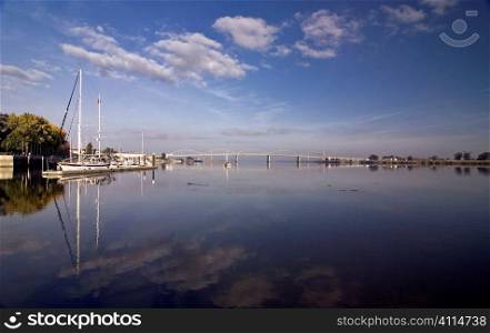 Wide-angle reflection of clouds on sea, marine and bridge in background