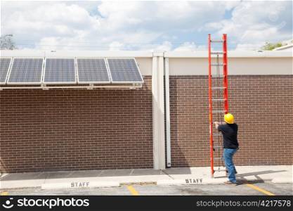 Wide angle view of a construction worker preparing to climb on to the roof of a building to work on solar panels.