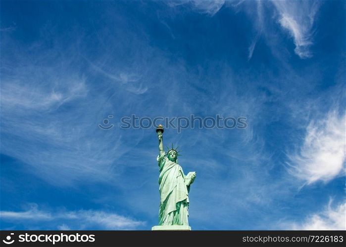 Wide-angle view of the Statue of Liberty against a cloudy blue sky, New York City.