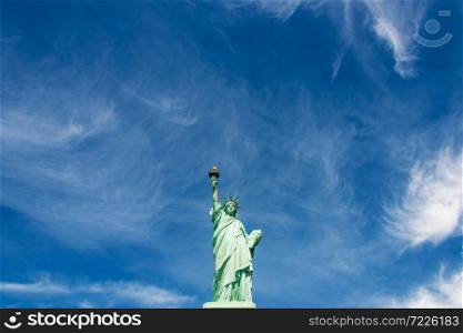 Wide-angle view of the Statue of Liberty against a cloudy blue sky, New York City.