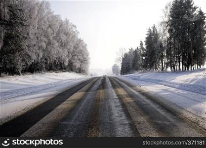 wide asphalt road in the winter season of the year, winter landscape with trees, mixed forest with features of the winter season. wide asphalt road