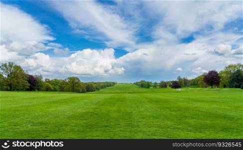 Wide grass filled view lined with trees in English parkland with dramatic sky. Wide parkland in England with dramatic sky