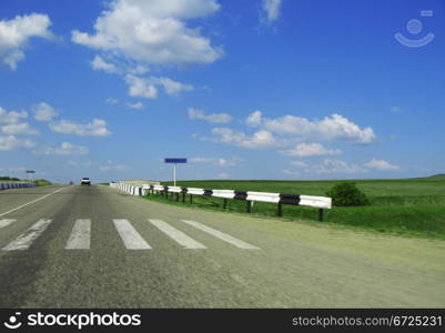 Wide highway and meadow. Clouds over and blue sky