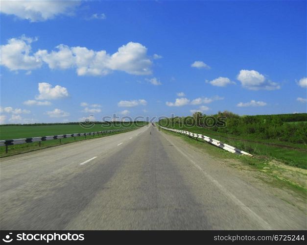 Wide highway and meadow. Clouds over and blue sky