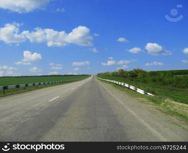 Wide highway and meadow. Clouds over and blue sky