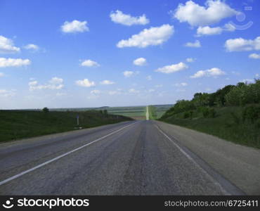 Wide highway and meadow. Clouds over and blue sky