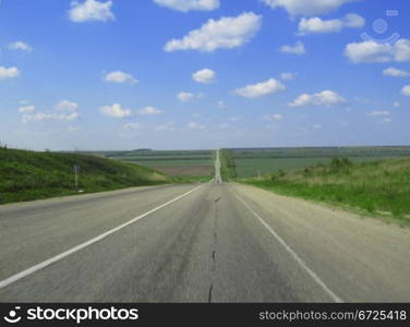 Wide highway and meadow. Clouds over and blue sky