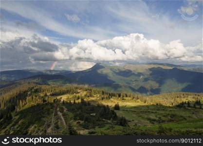Wide mountain spruces hill under clouds landscape photo. Nature scenery photography with rainbow on background. Ambient light. High quality picture for wallpaper, travel blog, magazine, article. Wide mountain spruces hill under clouds landscape photo