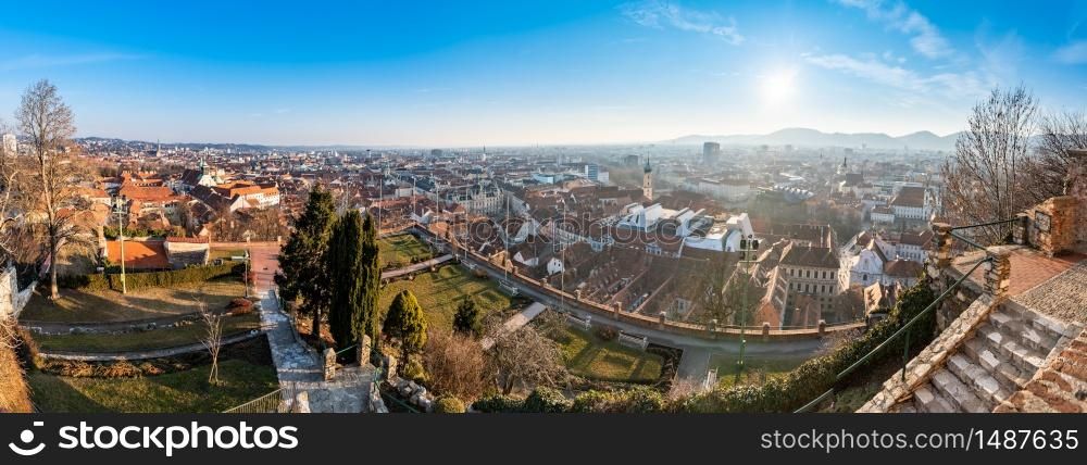 Wide panorama of Graz City, City rooftops, Mur river and city center, Schlossberg hill and clock tower Sun in winter, blue sky. Travel destination.. Wide panorama of Graz City from castle hill Schlossberg, Travel destination.