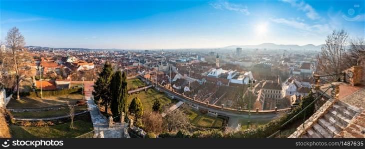 Wide panorama of Graz City, City rooftops, Mur river and city center, Schlossberg hill and clock tower Sun in winter, blue sky. Travel destination.. Wide panorama of Graz City from castle hill Schlossberg, Travel destination.