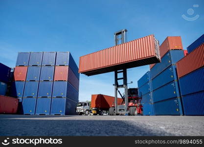 Wide shot of crane truck level up cargo container tank also show stack or layer of containers with different color, blue and brown with carrier truck as back of crane,  logistic and delivery concept.