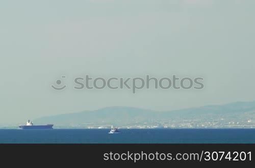 Wide shot of the calm sea in sunny day, some boats are sailing, big coastal city on the background.