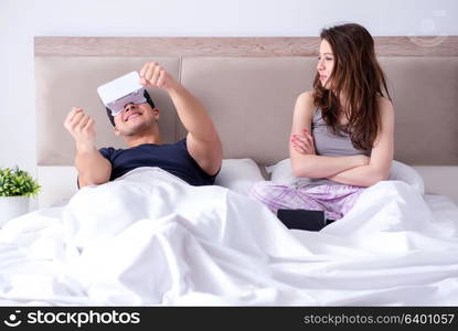 Wife and husband with virtual reality goggles in the bed