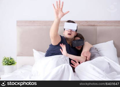 Wife and husband with virtual reality goggles in the bed