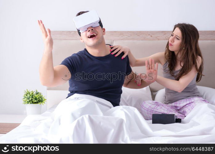 Wife and husband with virtual reality goggles in the bed