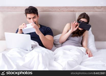 Wife and husband with virtual reality goggles in the bed