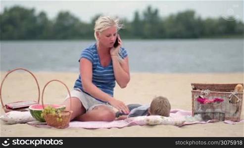Wife making a phone call while taking care of son at the beach.