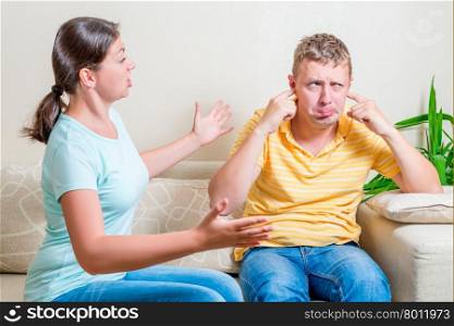wife scolds her husband sitting on a sofa in the living room