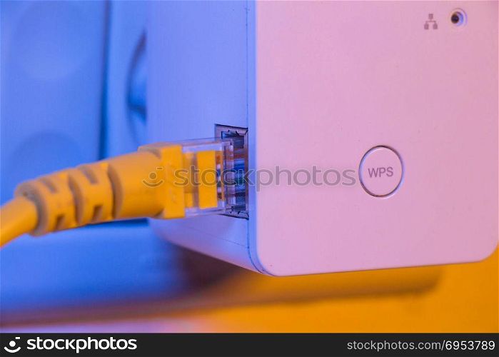 WiFi extender in electrical socket on the wall with ethernet cable plugged in. The device is in access point mode that help to extend wireless network in home or office.