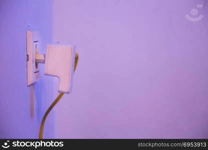 WiFi extender in electrical socket on the wall with ethernet cable plugged in. The device is in access point mode that help to extend wireless network in home or office.