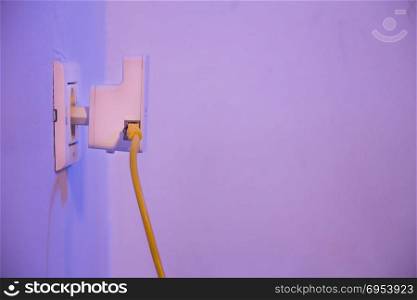WiFi extender in electrical socket on the wall with ethernet cable plugged in. The device is in access point mode that help to extend wireless network in home or office.