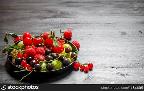 Wild berries in the old plate. On a black wooden background.. Wild berries in the old plate. On black wooden background.