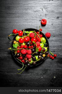 Wild berries in the old plate. On a black wooden background.. Wild berries in the old plate. On black wooden background.