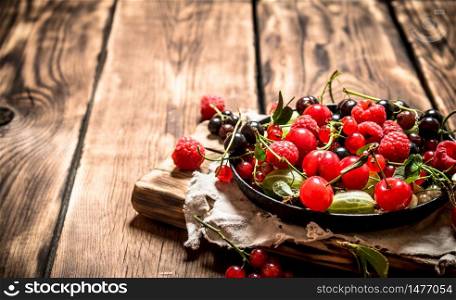 Wild berries in the old plate on the Board. On wooden background.. Wild berries in the old plate on the Board.