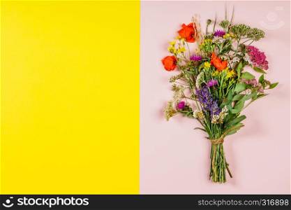 Wild flower bouquet on pink and yellow background. Top view, flat lay