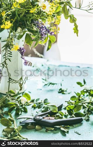 Wild flowers bunch in vase with pruner on table at window, front view. Home decor ideas