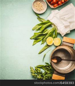 Wild garlic in paper with cooking pot and spoon, and ingredients on kitchen table background, top view, place for text. Healthy seasonal food and eating concept