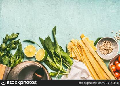 Wild garlic pasta cooking ingredients: pot with spoon, wild garlic,pasta noodles, pine nuts, tomatoes and seasoning on blue background, top view. Healthy seasonal food and eating concept