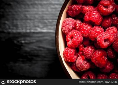 Wild raspberries in a bowl. On a black wooden background.. Wild raspberries in a bowl.
