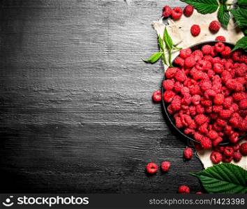 Wild raspberry with leaves on the old plate. On a black wooden background.. Wild raspberry with leaves on the old plate.
