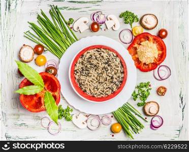 Wild rice dish and various vegetables and seasoning ingredients for tasty vegetarian cooking on light rustic wooden background, top view composing. Healthy eating and diet food concept.
