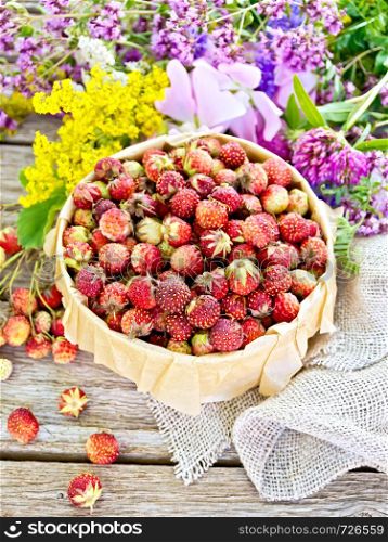 Wild ripe strawberries in a bark box with parchment, burlap and wild flowers on a wooden board background