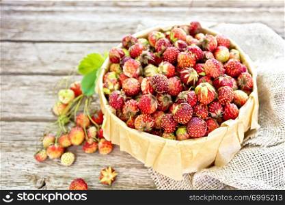 Wild ripe strawberries in a birch bark box with parchment, burlap on the background of old wooden boards