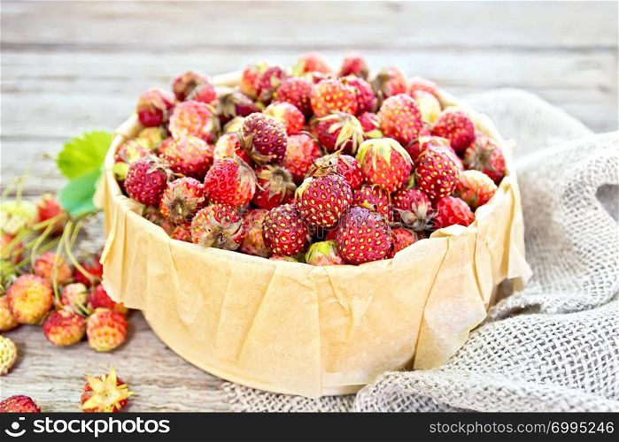 Wild ripe strawberries in a birch bark box with parchment on sackcloth against the background of old wooden boards