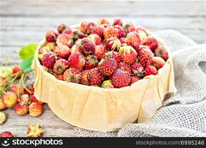Wild ripe strawberries in a birch bark box with parchment on sackcloth against the background of old wooden boards