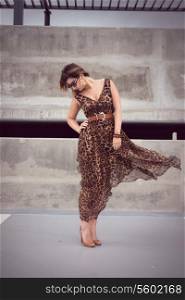 Wild woman dressed in animal print outfit maxi dress in urban concrete jungle with wind blowing her dress