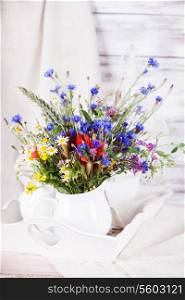 Wildflowers in white ceramic jug and cups on tray