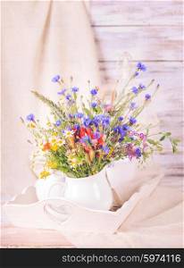 Wildflowers in white ceramic jug and cups on tray. Wildflowers in bottles