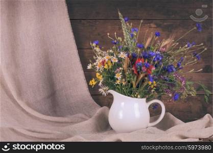 Wildflowers in white ceramic jug and cups on tray. Wildflowers in jug